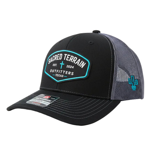 Black and gray cap with 'Sacred Terrain Outfitters' logo on a rock with grass background